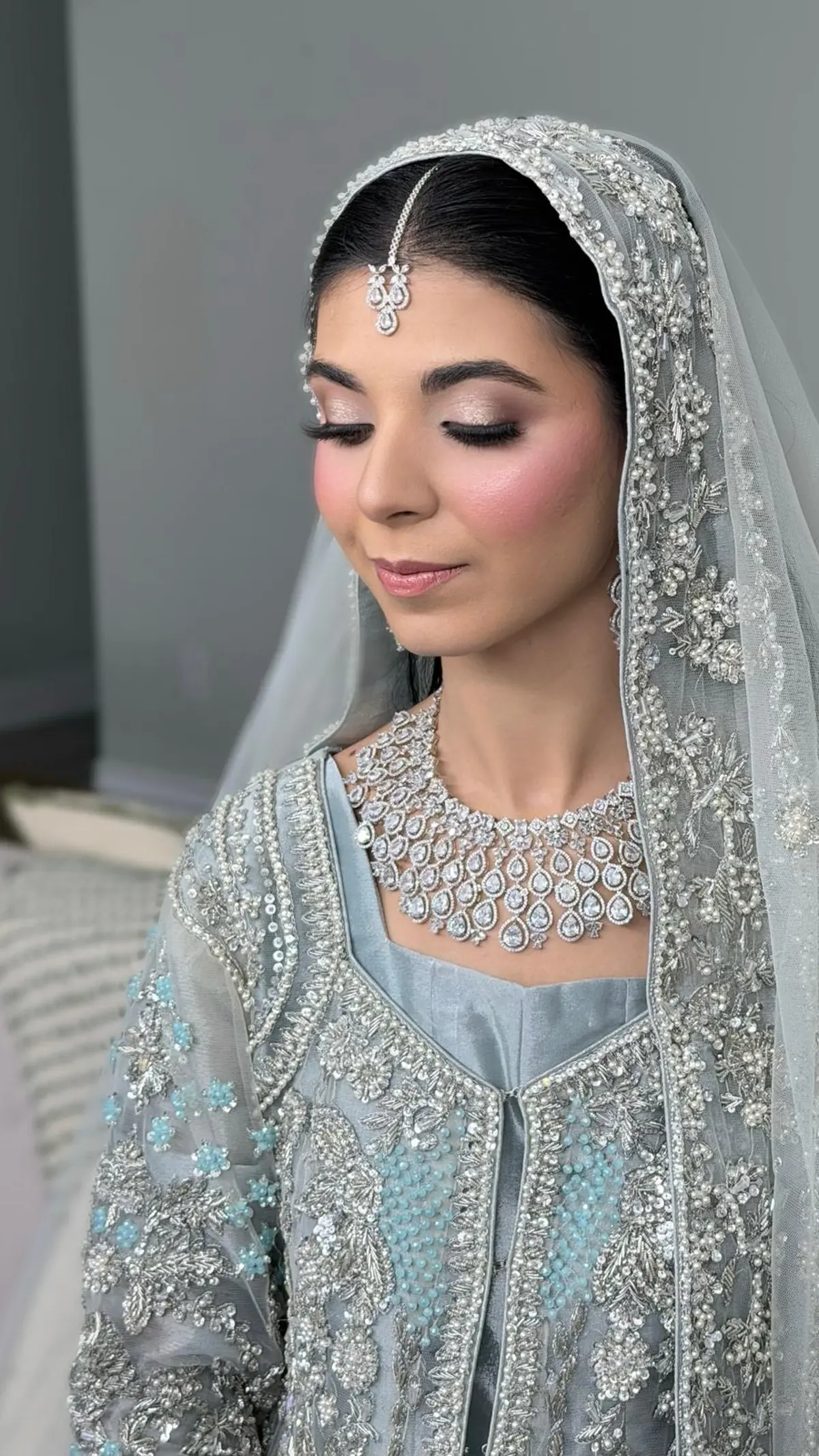 Bride in ice blue and silver with a diamond necklace and tikka, a pearl edged veil over a sleek centre part.