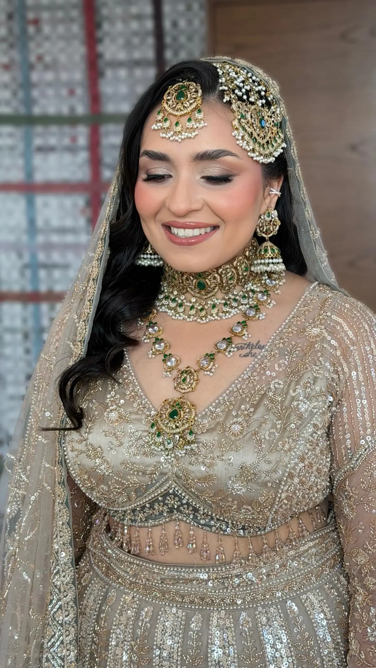 Bride in a champagne sequinned lehenga with an emerald and pearl choker, rani haar and jhoomar, hair in loose waves.